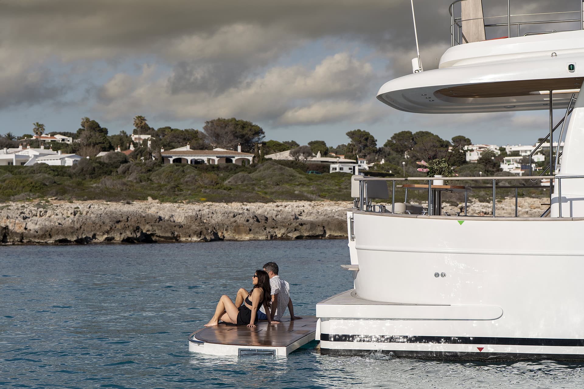 Pareja sentada junto al mar en la plataforma de baño sumergible de un Menorquín 48 FB