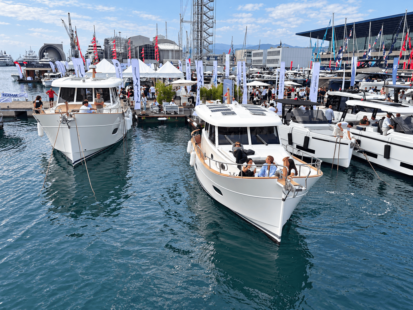 Dos Menorquín vistos de proa, con visitantes a bordo y el stand de Sasga Yachts al fondo en el puerto de Génova.